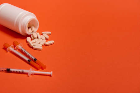 Studio shot of insulin syringes and pharmaceutical pills scattered from a white medicament container on orange background with copy space for medical ad for World Diabetes Awareness Day 14 November.の写真素材