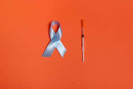 Medical concept 14 for November. Flat lay of insulin syringe and blue satin ribbon, symbolic bow color of World diabetes awareness day, isolated over orange colored background with copy space for adの写真素材