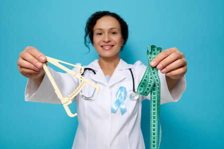 Health care and medical concept, metabolic syndrome disease. Soft focus on caliper and measuring tape in the hands of female doctor nutritionist endocrinologist wearing blue diabetes awareness ribbon.の写真素材