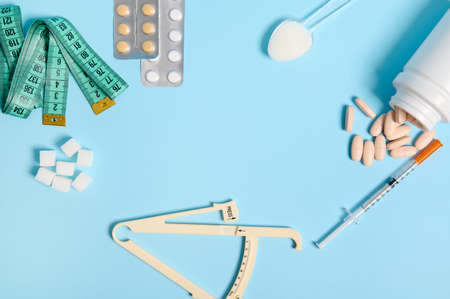 World Diabetes Awareness Day. Flat lay. White refined sugar, caliper, measuring tape, scattered pills, blister with medicines and insulin syringe with copy space at center on blue colored background.の写真素材