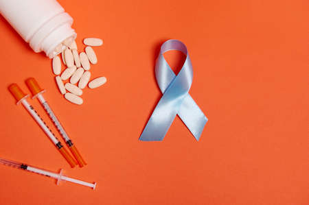 Flat lay of insulin syringes, pharmaceutical pills scattered from white medicament container and blue ribbon, symbol of World Diabetes Awareness Day 14 November. Medical concept for advertisementの写真素材