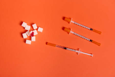 World diabetes day awareness concept, 14 November. Flat lay composition of insulin syringes and white sugar cubes with blood drop isolated over colored orange background with copy space for medical adの写真素材