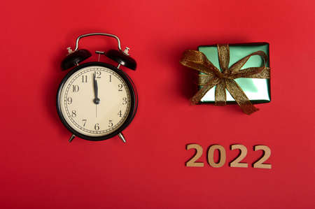 Flat lay of a black alarm clock with midnight on the dial, wooden numerals symbolizing the year 2022 and a Christmas present in shiny green wrapping gift paper with gold ribbon and bow. Copy spaceの写真素材