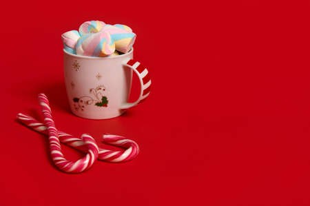 Studio shot of a mug of hot drink with marshmellows and candy canes on red colored background with copy space for Christmas adの写真素材