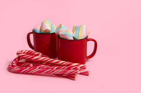 Coffee mug with marshmallows and candy canes on pink colored background. Christmas hot drink with desserts. Hot chocolate, cup of coffee cocoa. New year, merry christmas holiday celebrationの写真素材