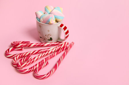 Beautiful minimalistic Christmas composition with hot chocolate drink decorated with marshmallows and striped lollipops, candy canes isolated over pink colored backgroud with copy space for adの写真素材