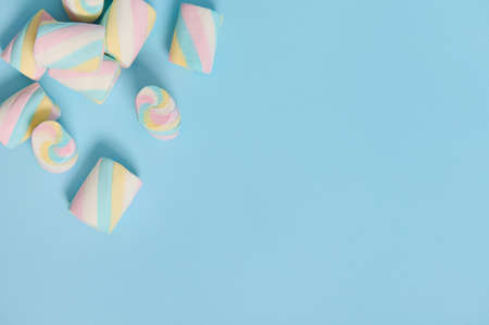 Colorful multi colored sweet marshmallows in the corner of a blue pastel background with copy space for advertising. Flat lay minimalistic compositionの写真素材