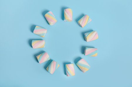 Colorful multi colored sweet sugary marshmallows laid out in the shape of circle on a blue pastel background . Food background with copy space for advertisement. Minimalistic style, designの写真素材