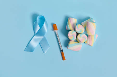 High angle view of marshmallows, blue satin awareness ribbon and insulin syringe laid out on pastel background with copy space for medical ad for 14 November, World Diabetes Awareness Day. Flat layの写真素材