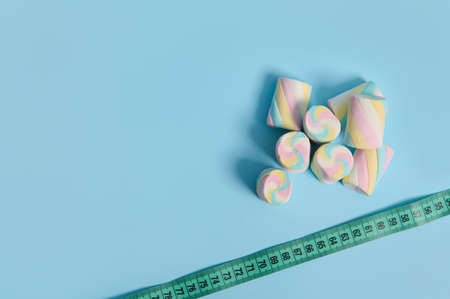 Top view of sweet colorful marshmallows and measuring tape on corner of blue background with copy space for medical ad. Link between overweight and unhealthy eating habits. World diabetes day conceptの写真素材