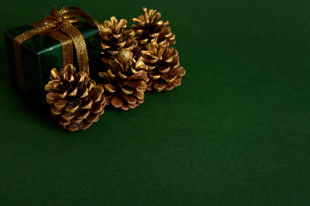 Close-up composition of golden pine cones and small luxury present in glitter green wrapping gift paper with golden bow in the corner of green background with copy space for New Year and Christmas adの写真素材