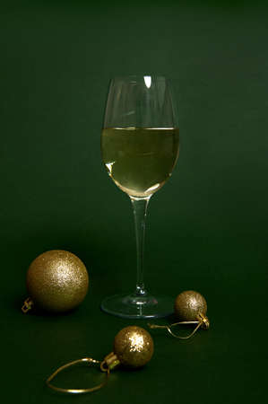 Glass with white wine on green background with gold spherical Christmas decorations, shiny balls. New year concept shot with soft shadow in monochrome and bi-color style for design and advertisementの写真素材