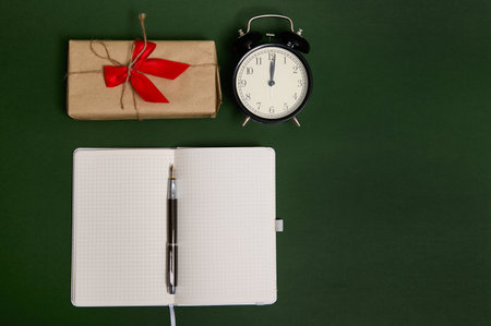 Flat lay composition with a pen on an opened notepad with empty blank sheets , alarm clock and a...