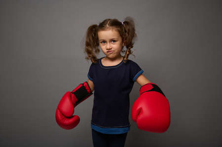 Cute Caucasian baby girl wearing red boxing gloves poses against gray wall background with copy space for advertisement for Boxing Dayの写真素材