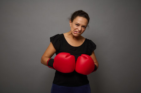 Strong concentrated African woman looks at camera posing against gray wall background with red...