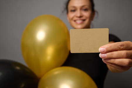 Focus on empty blank golden credit card in the hand of beautiful smiling woman holding black gold...