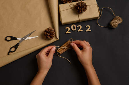 Preparing for Christmas. Women's hands tying cinnamon with a rope. Simple minimalistic gift wrapped...
