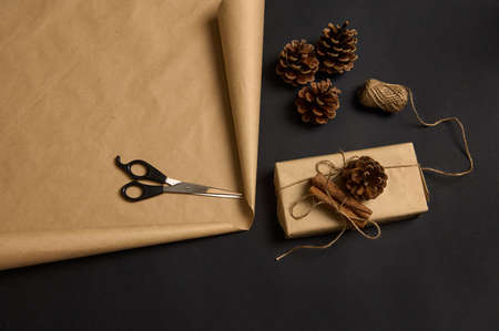 High angle view of Christmas present decorated with pine cone and tied cinnamons, wooden numerals 2022, scissors and rope on brown craft wrapping gift paper on black surface with a copy space for adの写真素材