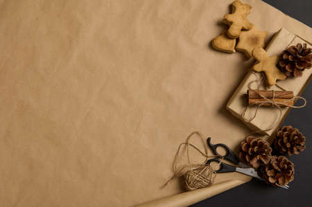Simple minimalistic Christmas composition with handmade gingerbread biscuits and present decorated with pine cone and tied cinnamon in a bow with rope on brown craft wrapping paper with copy ad spaceの写真素材