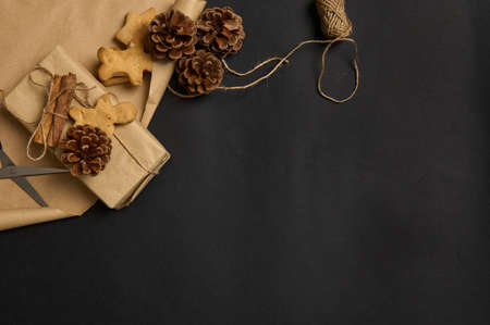 Simple minimalistic Christmas composition with handmade gingerbread biscuits and present decorated with pine cone and tied cinnamon in a bow with a rope on a brown craft wrapping paper with copy spaceの写真素材