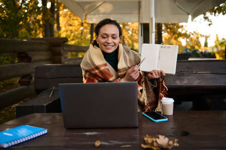 Pretty woman smiles showing with pen on blank blank page with to-do list during video conference on...