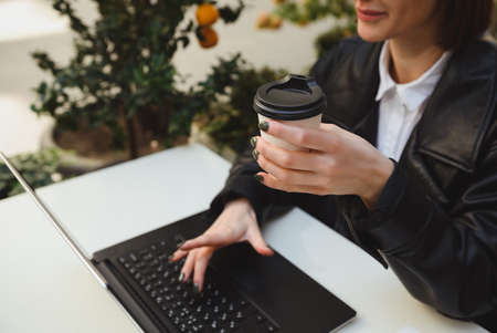 Soft focus on the hand holding takeaway paper mug, cardboard cup with hot drink, of a pretty woman...