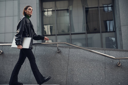 Portrait of modern, successful motivated self-confident freelancer young woman, walking with laptop...