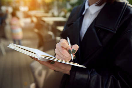 Close-up. Cropped image of unrecognizable young business woman holding a pen and notepad, writing, making notes.の写真素材