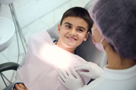 Pediatrician dentistry concept. Dental oral hygiene. Overhead view of European little boy smiling with beautiful toothy smile looking at medical assistant preparing him for regular dental check-upの写真素材