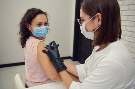Young woman wearing a protective medical mask receives antiviral vaccine against virus or flu at...