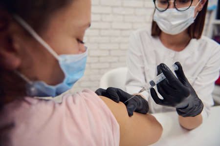 Dark-haired woman in medical protective mask being vaccinated with virus vaccine. Voluntary...