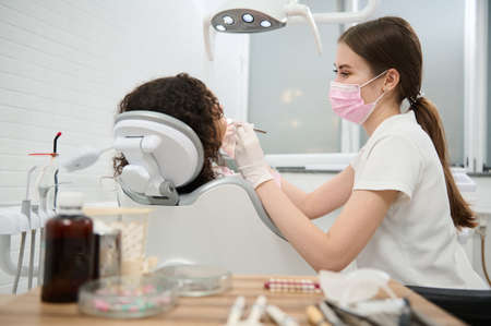 Young female dentist hygienist wearing protective medical mask examining dental clinic patients...