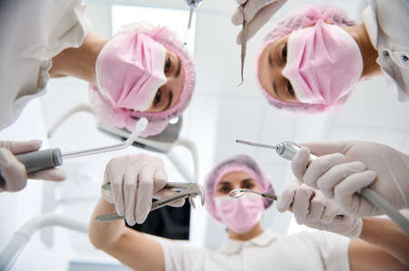 Focus on dental modern equipment and sterile stainless steel instruments in the hands of a group of...