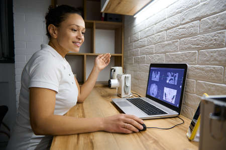 Woman doctor dentist sitting in front of a laptop with a panoramic x-ray of the human teeth and...