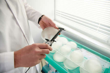 Close-up plastic surgeon hand measuring silicone breast implant size using a calliper. Mammoplasty,...