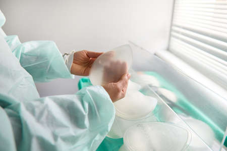 Breast silicone implant in surgeon hands on the background of medical samples of breast prosthesis of various sizes for aesthetic plastic surgery after resection due to breast cancer diseaseの写真素材
