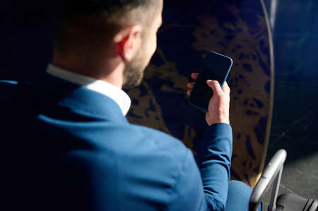 Rear view of a well-groomed attractive handsome bearded businessman in business casual suit using a...