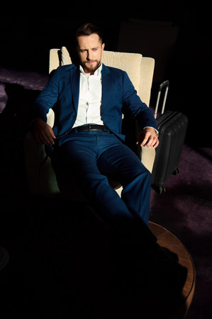 High angle view of a successful young businessman at business trip, relaxing on an armchair with outstretched crossed legs on an ottoman in lounge area of a luxury hotelの写真素材