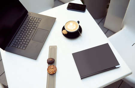 High angle view of delicious pastries on a white table next to a laptop and a cup of delicious...