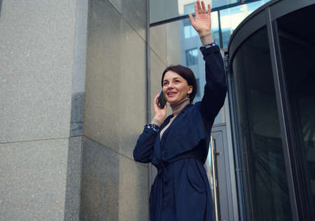 Self-confident beautiful woman smiling with toothy smile, talking on a mobile phone and raising her...