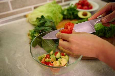 Top view of female hands cutting vegetables with kitchen knife and putting them on glass transparent...