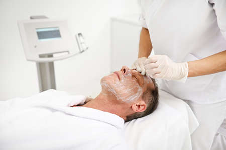 Mature 50 years old man receiving moisturizing revitalizing rejuvenating anti-aging beauty treatment in modern wellness spa clinicの写真素材