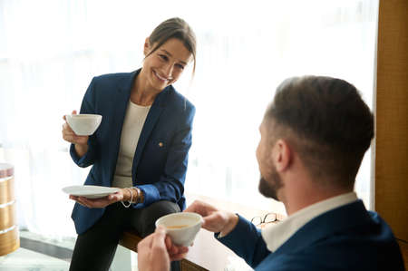 Charming young woman in business suit sitting at table in hotel room and smiles sweetly while...