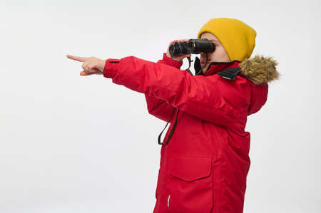 Studio shot of a curious school boy, adventurer, explorer in warm bright clothes looking through...