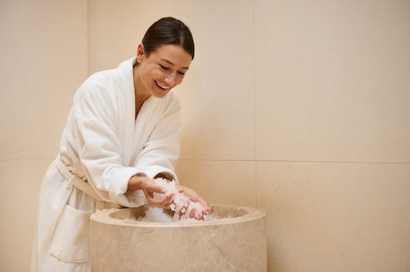 Charming middle aged dark-haired European woman dressed in white terry bathrobe resting at wellness spa, holding ice pieces in her hands. Youth, freshness, body treatment and recreation concept.の写真素材