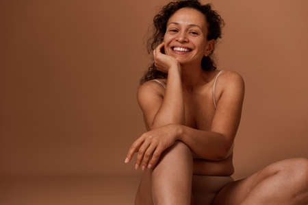 Self-confident beautiful middle aged woman in beige underwear, smiles toothy smile looking at camera. Body positivity, self-acceptance and body love conceptの写真素材