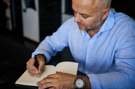 High angle view of a middle-aged European man writing in a notebook, planning projects, and making notes in a diary.の写真素材