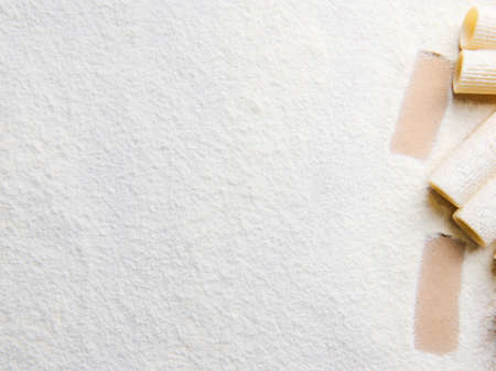 Flat lay composition with whole wheat Italian pasta - uncooked tortiglioni- in the corner of a white...
