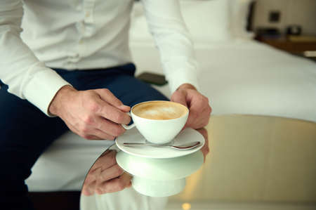 Close-up of a white ceramic cup on a saucer, with delicious coffee drink, cappuccino in the hands of...