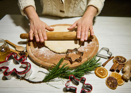 Unrecognizable chef woman rolling out dough with a rolling pin on a wooden board, preparing...